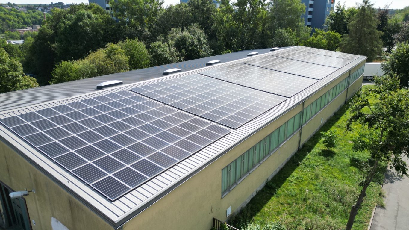 140kWp Dachanlage in Hof Dach mit Solarpanelen auf einem Gebäude, umgeben von Bäumen und Grünflächen.